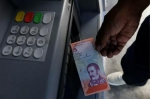 8月20日，在委内瑞拉首都加拉加斯，一名男子从ATM机中取出一张新货币“主权玻利瓦尔”。新华社发（格雷戈里奥·特兰摄） - News.Sina.com.Cn