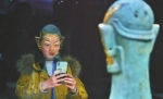 三星堆发现九十周年纪念特展，一位嘉宾拍摄戴金面具青铜人头像，倒影映在嘉宾脸上，像是戴上了一个面具。 本报记者杨树摄(视觉四川) - Sc.Chinanews.Com.Cn